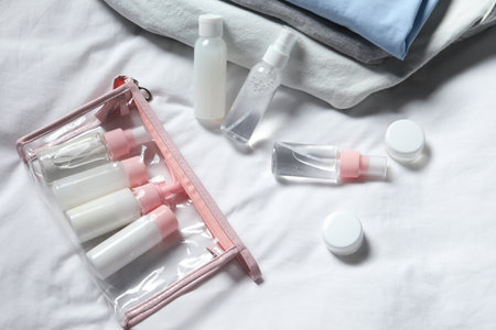 Cosmetic travel kit. Plastic bag with small containers of personal care products on bedの写真素材