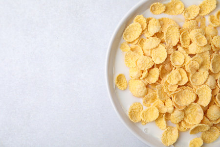 Breakfast cereal. Corn flakes and milk in bowl on light gray table, top view. Space for text