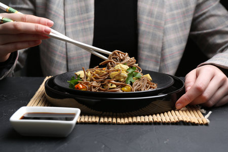 Stir-fry. Woman eating tasty noodles with meat and vegetables at dark textured table, closeupの写真素材
