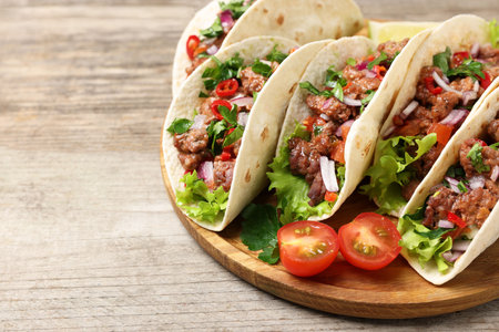 Delicious tacos with meat and vegetables on wooden table, closeup. Space for textの写真素材
