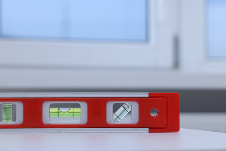 Red building level on white windowsill indoors, closeup