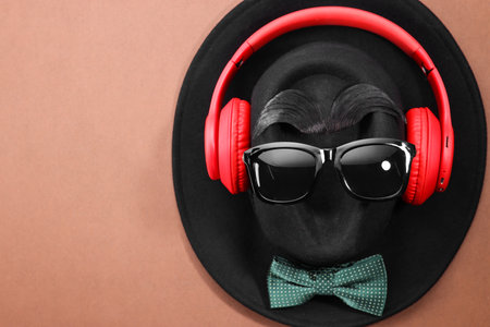 Man's face made of artificial mustache, sunglasses and hat on brown background, top view. Space for textの写真素材