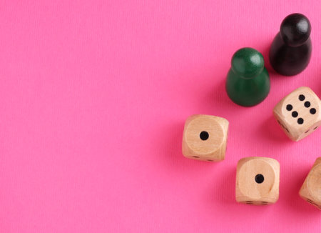 Wooden dices and color game pieces on pink background, flat lay. Space for textの写真素材