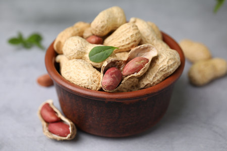 Fresh unpeeled peanuts in bowl on gray table, closeup