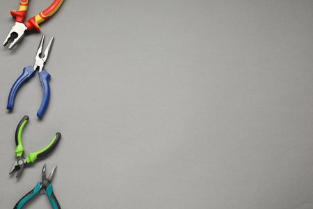 Different pliers on gray background, flat lay. Space for text