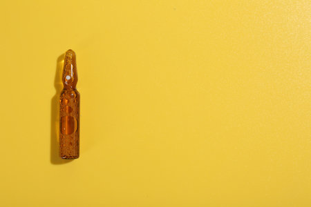 Glass ampoule with liquid on yellow background, top view. Space for text