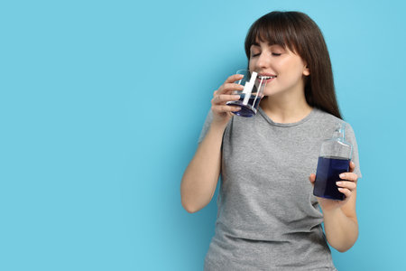 Young woman using mouthwash on light blue background, space for textの写真素材
