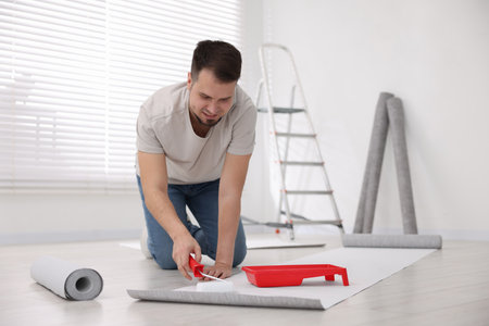 Man applying glue onto wallpaper sheet in roomの写真素材