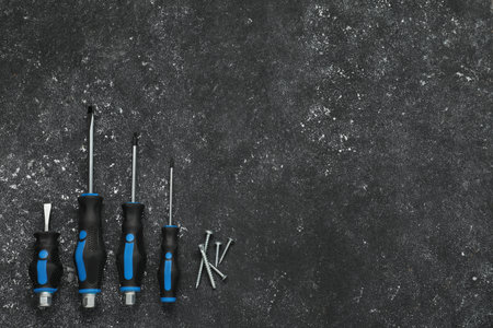 Set of screwdrivers and screws on gray table, top view. Space for text
