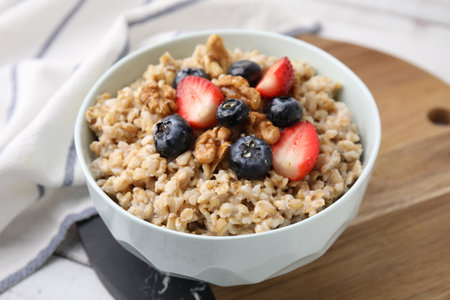 Tasty oatmeal with strawberries, blueberries and walnuts in bowl on white wooden table, closeupの写真素材