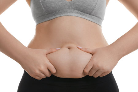 Woman touching belly fat on white background, closeup. Overweight problemの写真素材