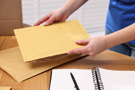 Post office worker packing parcel at wooden table indoors, closeup