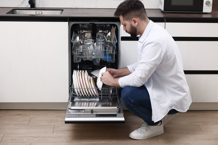 Man loading dishwasher with dirty plates indoorsの写真素材