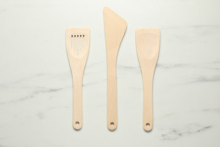 Different wooden spatulas on white marble table, flat lay