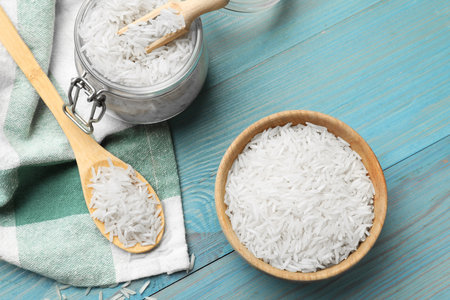 Raw basmati rice in bowl, jar, spoon and scoop on light blue wooden table, flat layの写真素材