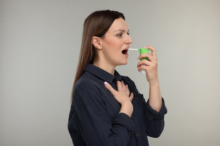 Woman using throat spray on grey backgroundの写真素材