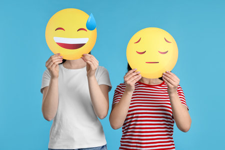 People covering faces with emoticons on light blue backgroundの写真素材