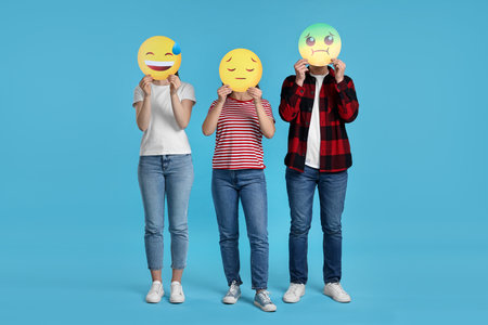 People covering faces with emoticons on light blue backgroundの写真素材