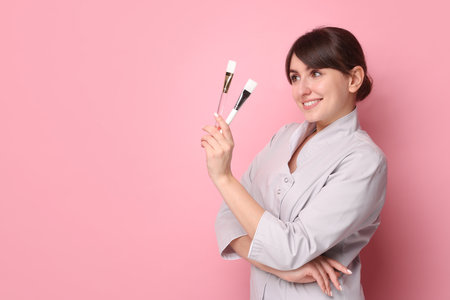 Cosmetologist with cosmetic brushes on pink background, space for textの写真素材