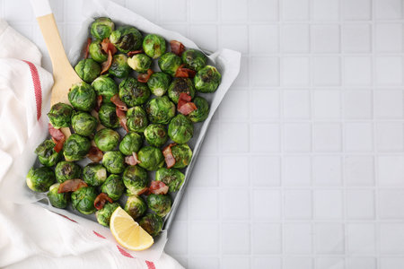 Delicious roasted Brussels sprouts, bacon and lemon in baking dish on white tiled table, top view. Space for textの写真素材