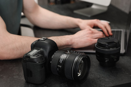 Camera on dark table, closeup. Photographer working with computer indoors, selective focusの写真素材