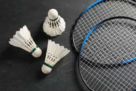 Feather badminton shuttlecocks and rackets on gray textured table, flat lay