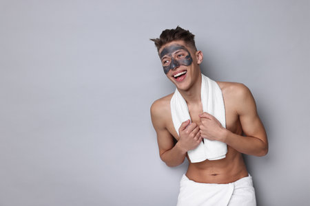 Handsome man with clay mask on his face against light grey background. Space for textの写真素材