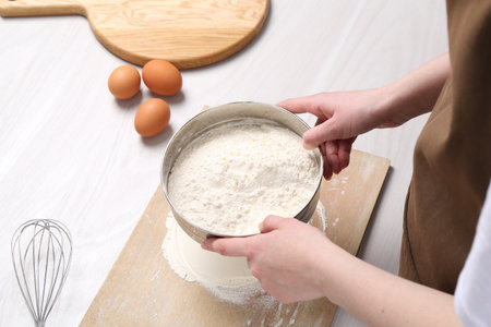 Woman sieving flour at white wooden table, above view