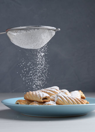 Woman with sieve sprinkling powdered sugar onto cookies at white wooden table, closeupの写真素材
