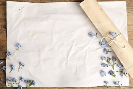 Beautiful forget-me-not flowers and sheets of old parchment paper on wooden table, top viewの写真素材