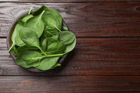 Fresh spinach leaves in bowl on wooden table, top view. Space for textの写真素材