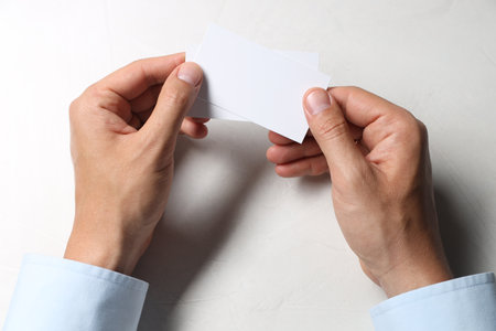 Man holding blank cards at white table, top view. Mockup for designの写真素材