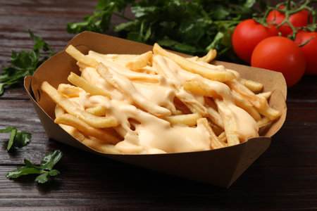 Tasty potato fries, cheese sauce in paper container and products on wooden table, closeupの写真素材
