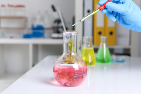 Laboratory analysis. Woman dripping liquid into flask at white table, closeupの写真素材