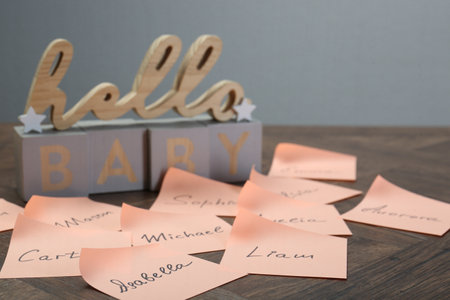 Cubes with phrase Hello Baby and paper stickers with different names on wooden table, closeup. Choosing baby's nameの写真素材