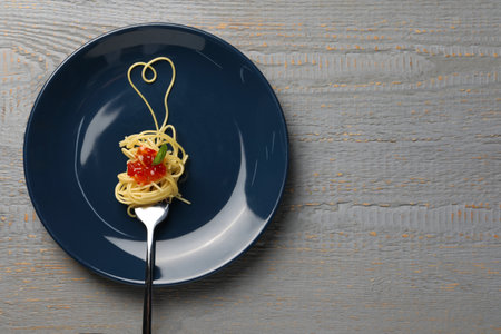 Heart made with spaghetti and fork on gray wooden table, top view. Space for text