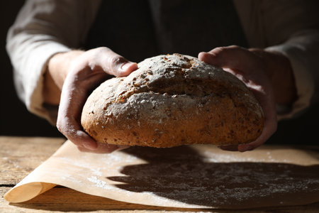 Man breaking loaf of fresh bread at wooden table, closeupの写真素材