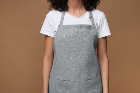Woman wearing kitchen apron on brown background, closeup. Mockup for designの写真素材