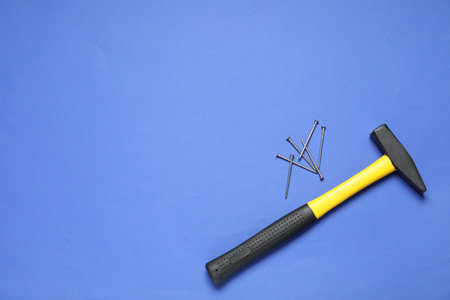 Hammer and metal nails on blue background, top view. Space for text