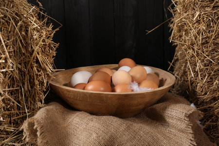 Fresh chicken eggs in bowl among dried straw bales