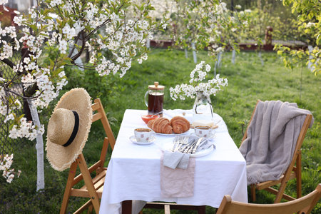Stylish table setting with beautiful spring flowers, tea and croissants in garden
