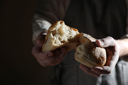 Man breaking loaf of fresh bread on dark background, closeupの写真素材