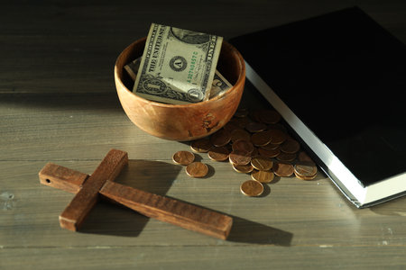 Donate and give concept. Bowl with coins, dollar banknotes, cross and Bible on wooden tableの写真素材