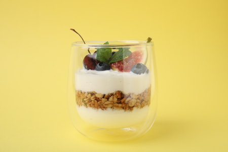 Glass with yogurt, berries and granola on yellow background