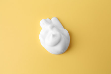 Sample of body care cream on yellow background, top view