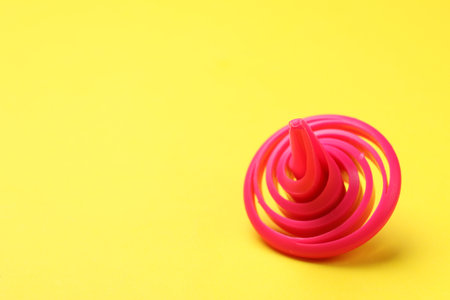 One pink spinning top on yellow background, closeup. Space for textの写真素材