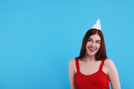 Happy woman in party hat on light blue background, space for textの写真素材