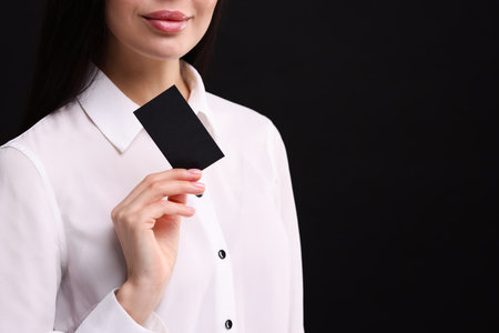 Woman holding blank business card on black background, closeup. Space for textの写真素材