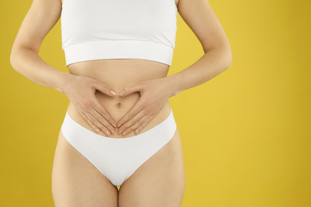 Gynecology. Woman in underwear making heart with her hands on yellow background, closeup. Space for textの写真素材