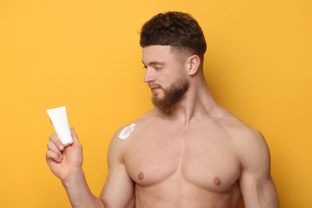 Handsome man with moisturizing cream on orange backgroundの写真素材